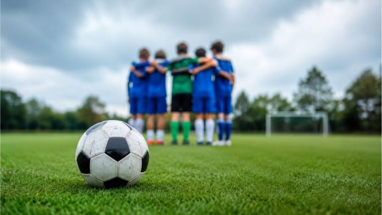 Soccer ball on a grassy field with young players gathered in a team huddle before practice